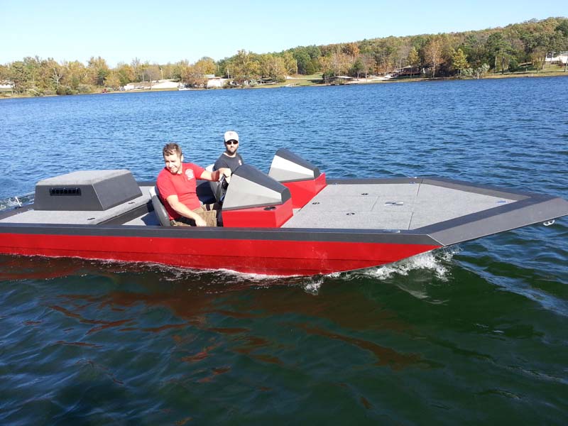 two men driving a red boat on a lake